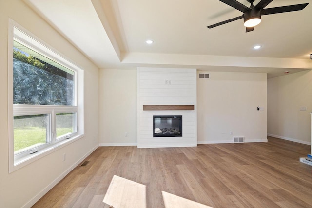 unfurnished living room featuring a large fireplace, ceiling fan, light hardwood / wood-style flooring, and plenty of natural light