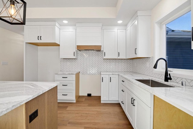 kitchen featuring light stone counters, white cabinets, decorative light fixtures, and sink