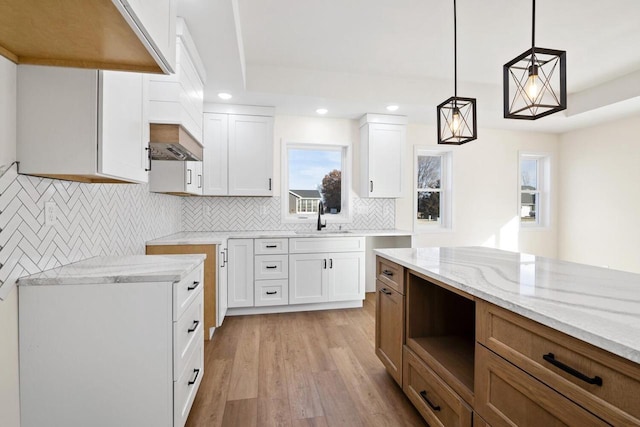 kitchen featuring sink, white cabinetry, light stone counters, and hanging light fixtures