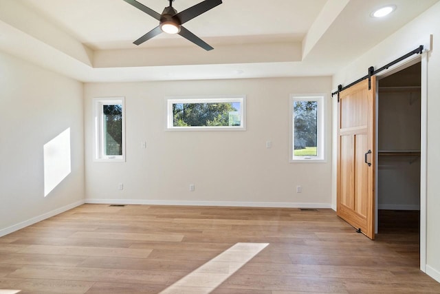 unfurnished bedroom with a raised ceiling, a closet, a barn door, a walk in closet, and ceiling fan