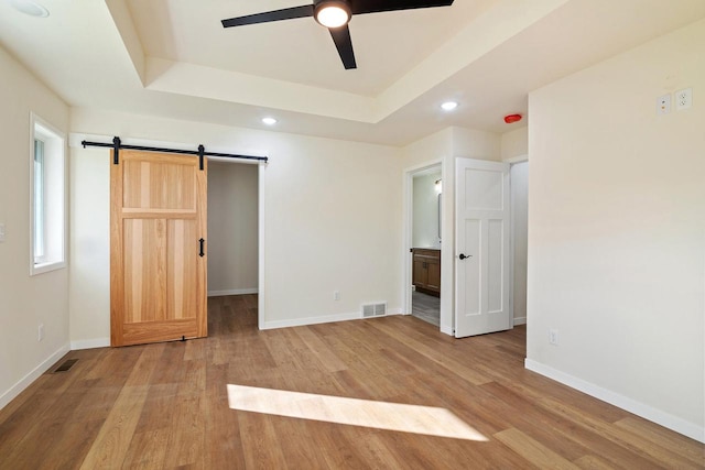 unfurnished bedroom featuring ensuite bathroom, ceiling fan, a barn door, and a tray ceiling