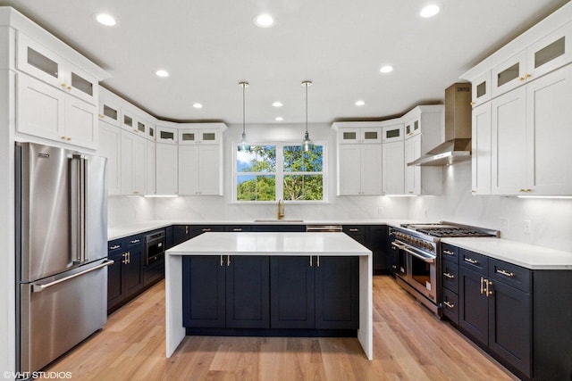 kitchen with light wood-type flooring, wall chimney exhaust hood, premium appliances, and pendant lighting