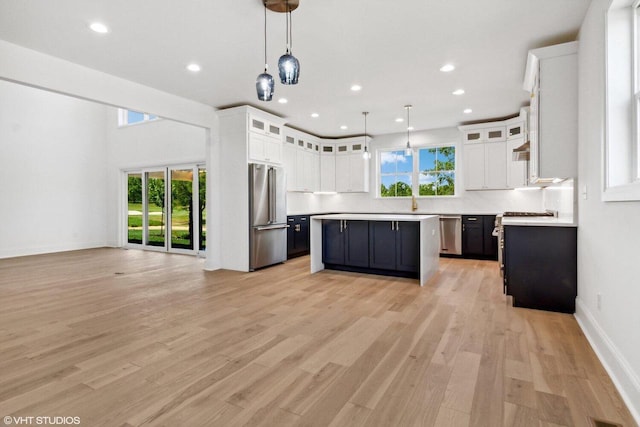 kitchen with stainless steel appliances, white cabinets, light hardwood / wood-style floors, and a center island