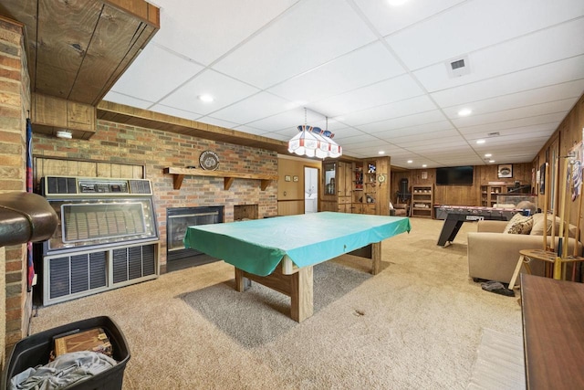 rec room with a drop ceiling, wooden walls, light colored carpet, and a brick fireplace