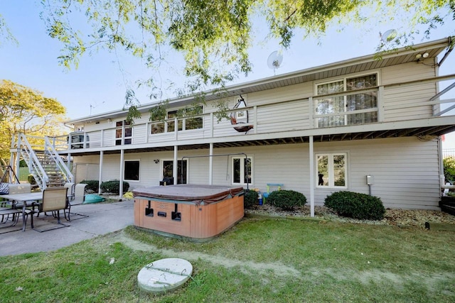 rear view of property featuring a lawn, a patio, and a hot tub