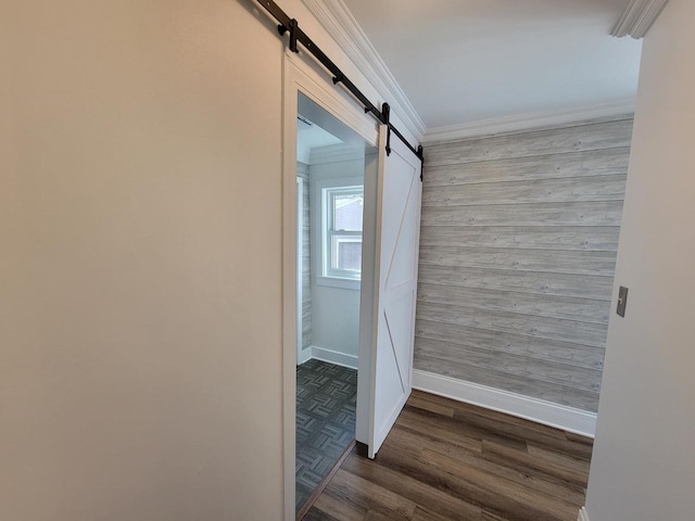 hallway with crown molding, a barn door, wooden walls, and dark hardwood / wood-style flooring