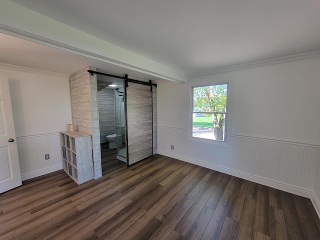 unfurnished bedroom featuring ornamental molding, dark hardwood / wood-style floors, a barn door, and connected bathroom