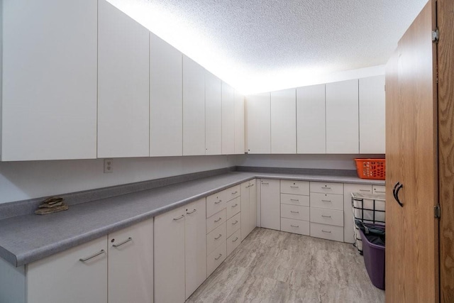 kitchen featuring a textured ceiling, light hardwood / wood-style flooring, and white cabinets