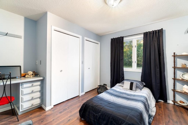 bedroom featuring a textured ceiling, two closets, and dark hardwood / wood-style flooring