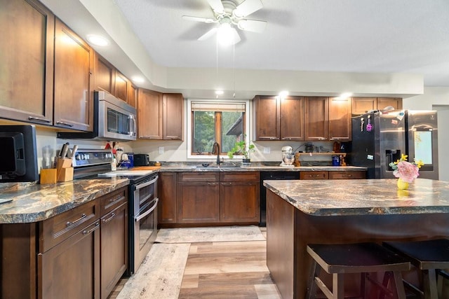 kitchen featuring sink, light hardwood / wood-style flooring, stainless steel appliances, dark stone countertops, and a kitchen bar