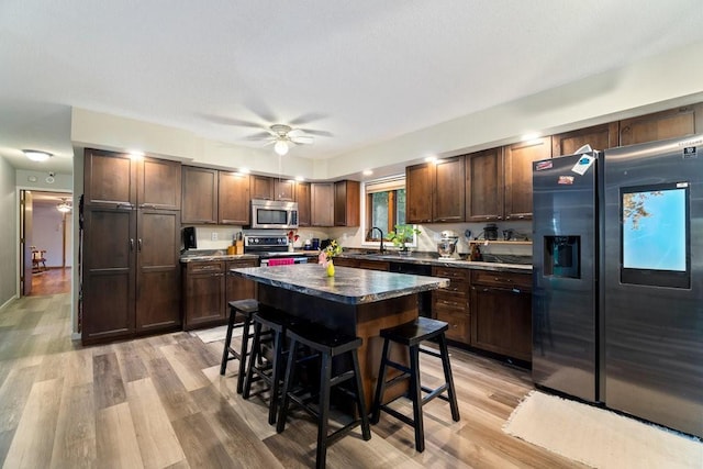 kitchen featuring ceiling fan, a kitchen island, appliances with stainless steel finishes, light wood-type flooring, and a kitchen bar