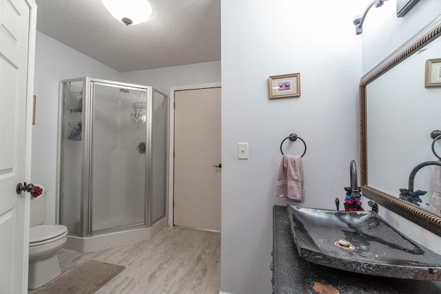 bathroom with vanity, a textured ceiling, hardwood / wood-style flooring, walk in shower, and toilet