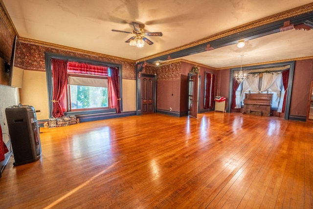 unfurnished living room with ornamental molding, wood-type flooring, and ceiling fan with notable chandelier