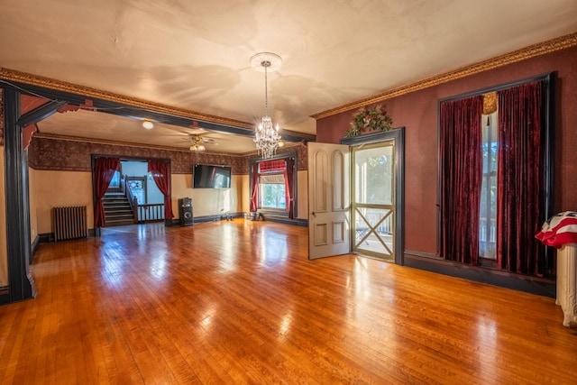 unfurnished living room featuring crown molding, wood-type flooring, radiator heating unit, and ceiling fan with notable chandelier