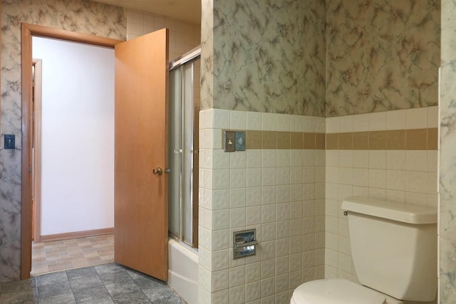 bathroom featuring enclosed tub / shower combo, tile walls, and toilet