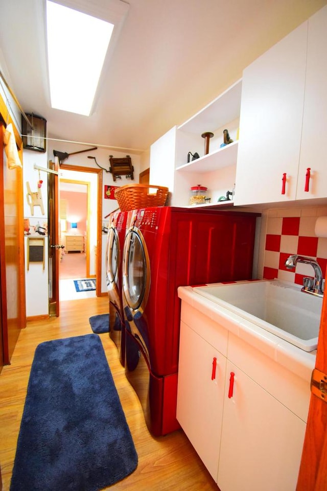 clothes washing area featuring cabinets, sink, washing machine and clothes dryer, and light hardwood / wood-style flooring