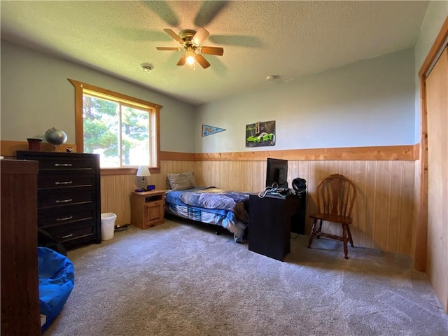 carpeted bedroom with a textured ceiling, wood walls, and ceiling fan