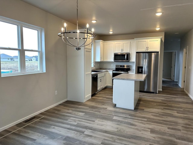 kitchen featuring white cabinets, hanging light fixtures, appliances with stainless steel finishes, a kitchen island, and wood-type flooring