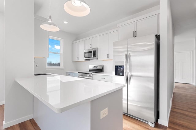 kitchen featuring stainless steel appliances, light hardwood / wood-style flooring, hanging light fixtures, and white cabinets