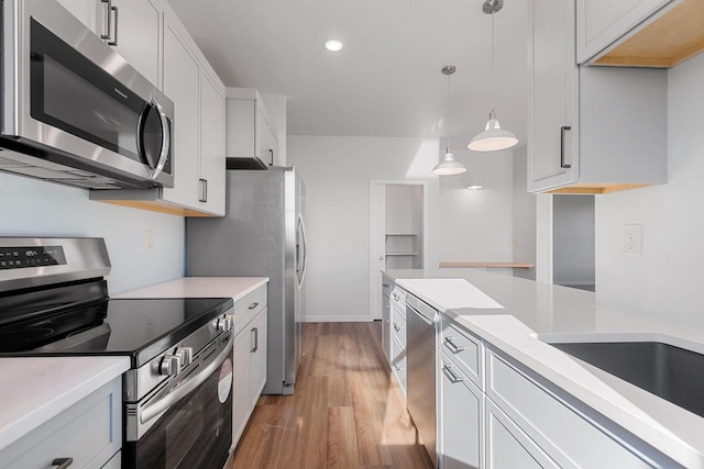 kitchen featuring stainless steel appliances, hardwood / wood-style flooring, white cabinets, and decorative light fixtures