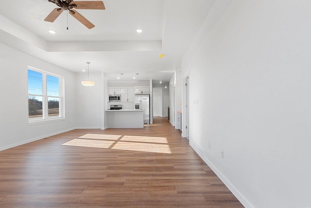 unfurnished living room with ceiling fan, wood-type flooring, and a raised ceiling