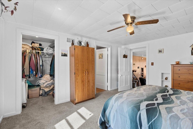 bedroom with a closet, light colored carpet, a walk in closet, and ceiling fan