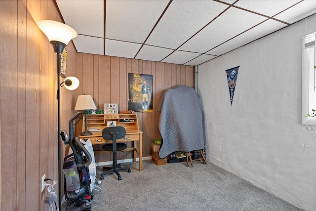 carpeted office featuring a paneled ceiling and wood walls