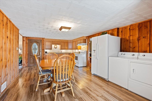 dining room with light wood-type flooring, wood walls, sink, and washing machine and dryer