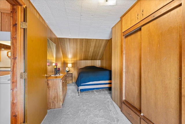 carpeted bedroom with lofted ceiling, wood walls, a closet, and washer / dryer