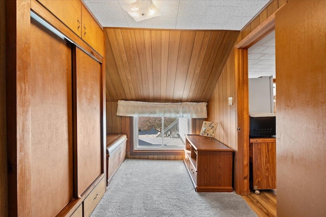 interior space with wooden ceiling, vaulted ceiling, wooden walls, and light carpet