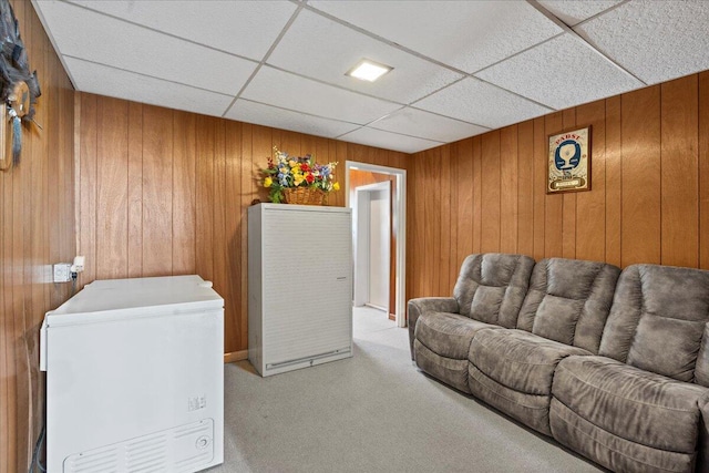 carpeted living room featuring wood walls and a drop ceiling