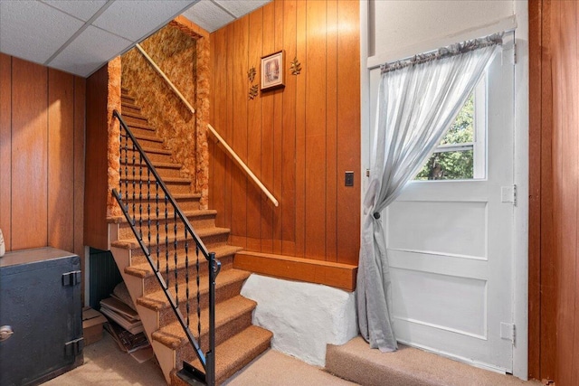 staircase with wood walls, carpet flooring, and a paneled ceiling