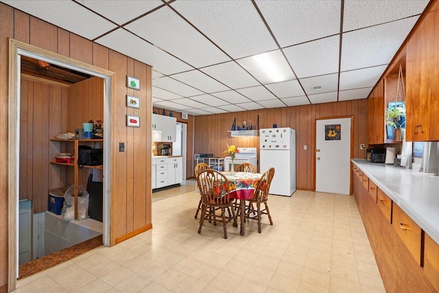 dining space featuring a drop ceiling and wooden walls