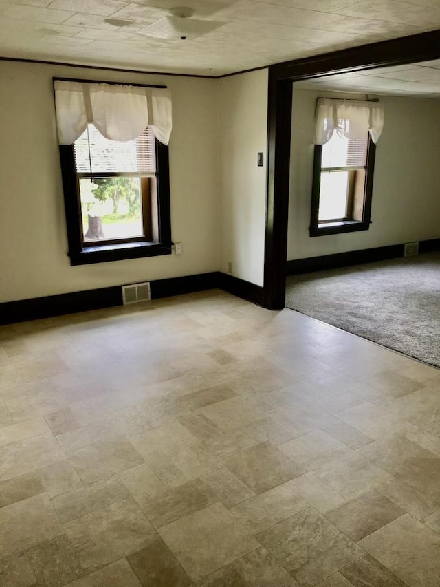 unfurnished room with plenty of natural light, light colored carpet, and beamed ceiling