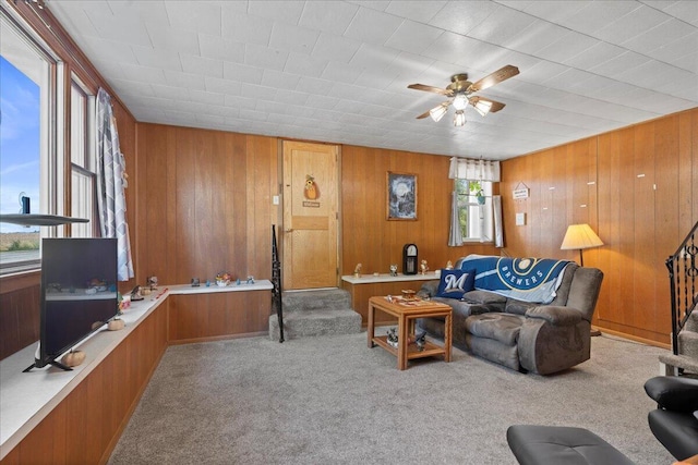 carpeted living room with ceiling fan and wood walls