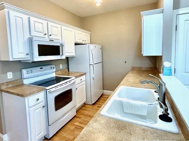 kitchen with light hardwood / wood-style floors, white cabinetry, white appliances, and sink