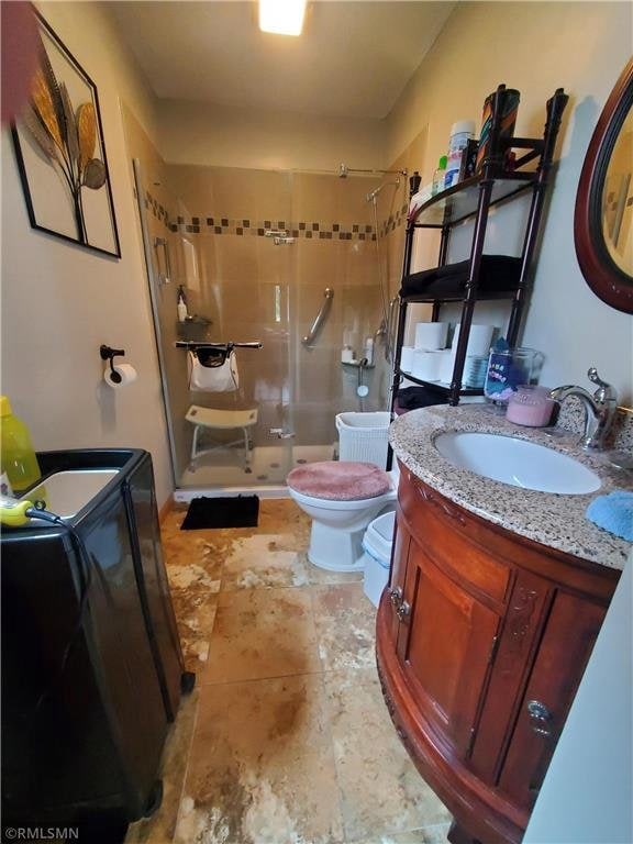 bathroom featuring washing machine and clothes dryer, tiled shower, vanity, and toilet