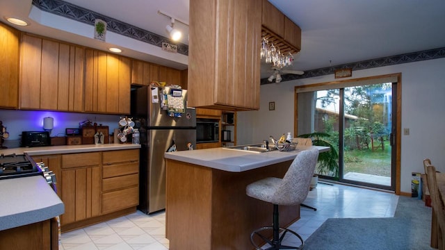 kitchen featuring stainless steel refrigerator, a kitchen island with sink, black microwave, sink, and a kitchen bar