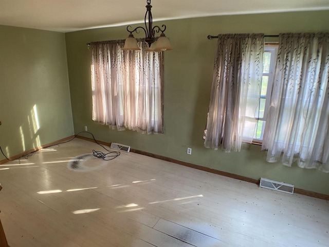 empty room featuring wood-type flooring and a chandelier