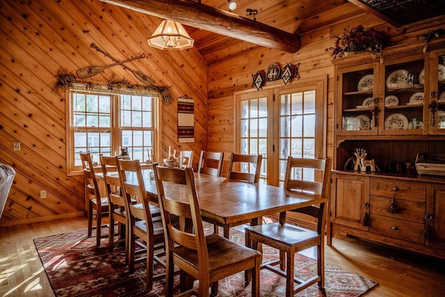 dining room with a wealth of natural light, vaulted ceiling with beams, wood walls, and hardwood / wood-style flooring