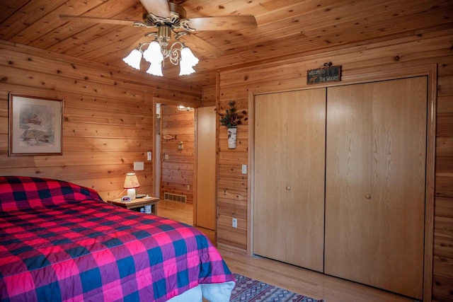 bedroom featuring ceiling fan, wooden walls, light hardwood / wood-style flooring, a closet, and wooden ceiling