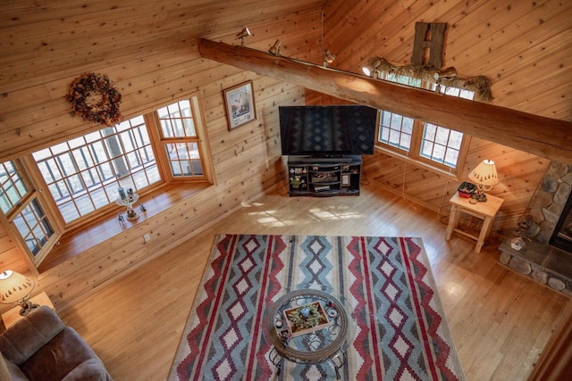 unfurnished living room featuring hardwood / wood-style flooring, a stone fireplace, wooden walls, and high vaulted ceiling