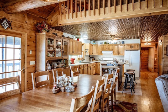 dining area featuring ceiling fan, beamed ceiling, sink, wooden walls, and light hardwood / wood-style flooring