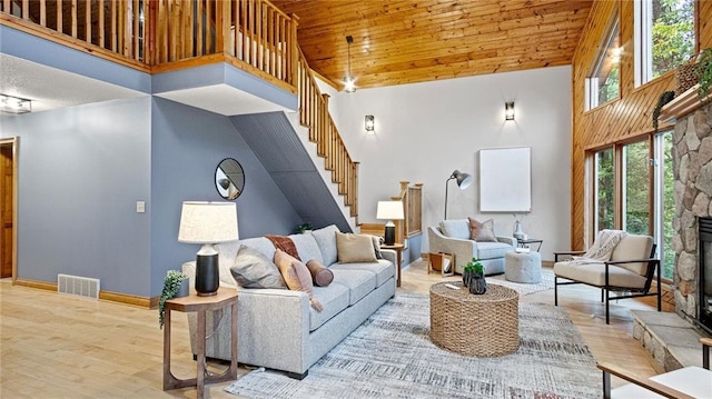 living room featuring wooden ceiling, a stone fireplace, light hardwood / wood-style flooring, and high vaulted ceiling