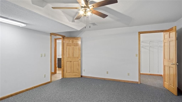 unfurnished bedroom featuring a textured ceiling, carpet flooring, ceiling fan, and a walk in closet