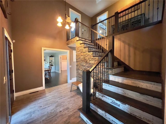 stairway with a high ceiling, a chandelier, and wood-type flooring