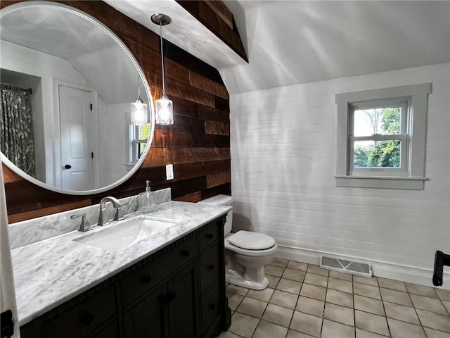 bathroom with lofted ceiling, wooden walls, vanity, tile patterned flooring, and toilet