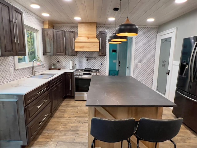 kitchen with light hardwood / wood-style flooring, decorative light fixtures, sink, stainless steel appliances, and premium range hood