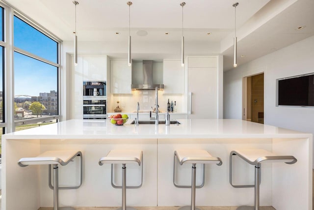 kitchen featuring decorative light fixtures, wall chimney exhaust hood, a kitchen breakfast bar, and white cabinetry