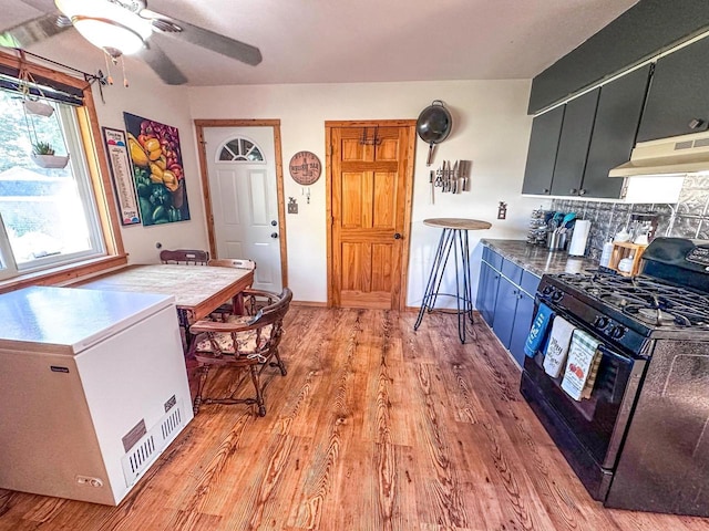 kitchen featuring decorative backsplash, light hardwood / wood-style floors, fridge, black gas stove, and extractor fan